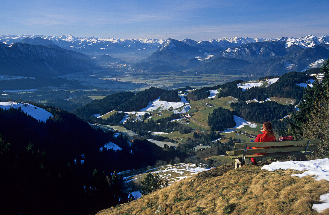 young lady sitting at vista bank on Karspitze, view to the valley of Inn and the snow-covered mountains of Zillertal and Rofan range, Chiemgau range, Chiemgau, Upper Bavaria, Bavaria, Germany