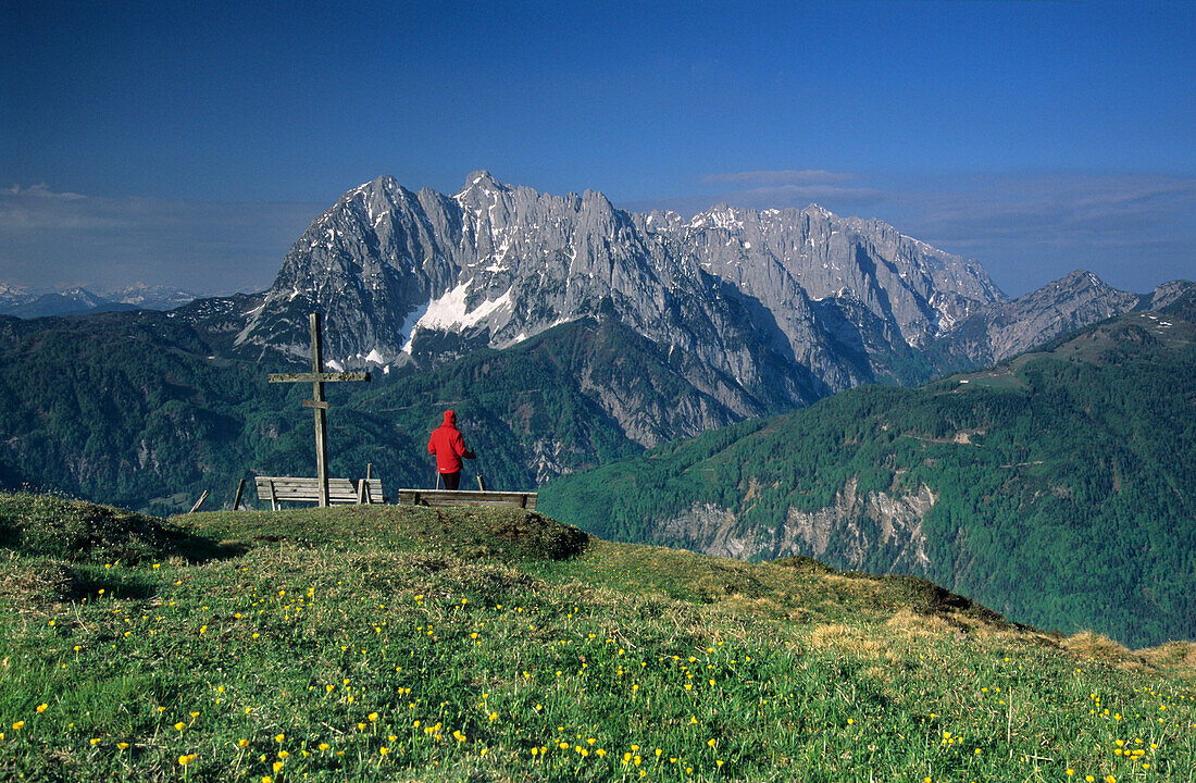 Hiker near summit cross of mount Schnappen, view to Wilder Kaiser range, Kaiser range, Tyrol, Austria