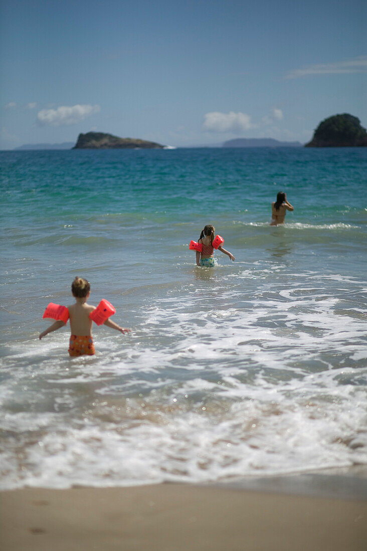 Mutter mit Töchtern (5 und 2,5 Jährige mit Schwimmhilfen), baden in Wellen am Hahei Beach, bei Hahei, Ostküste, Coromandel Peninsula, Nordinsel, Neuseeland