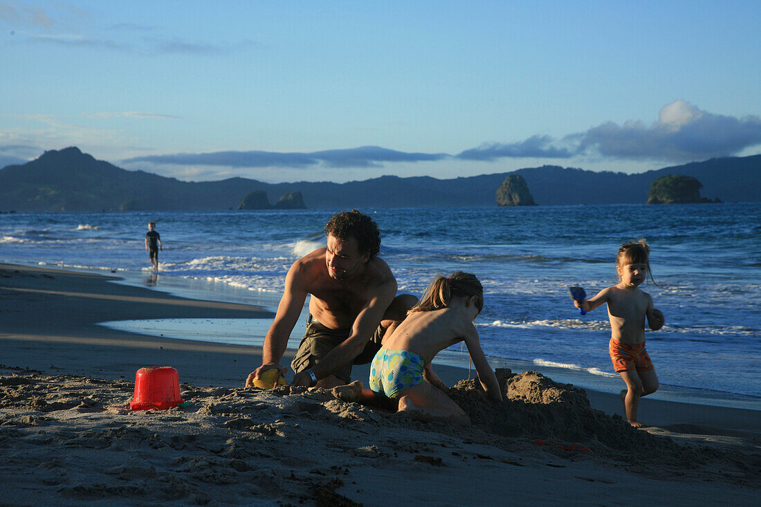 Vater mit Töchtern, buddeln im Sand, abends am Hahei Beach, bei Hahei, Ostküste, Coromandel Peninsula, Nordinsel, Neuseeland
