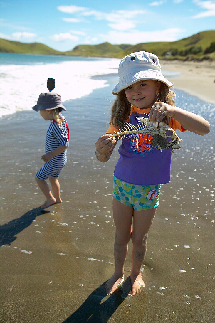 Mädchen mit Fischgräte, spielen am Strand, in Sonnenschutzkleidung, Strand von Port Jackson, Nordspitze der Coromandel Peninsula, Nordinsel, Neuseeland