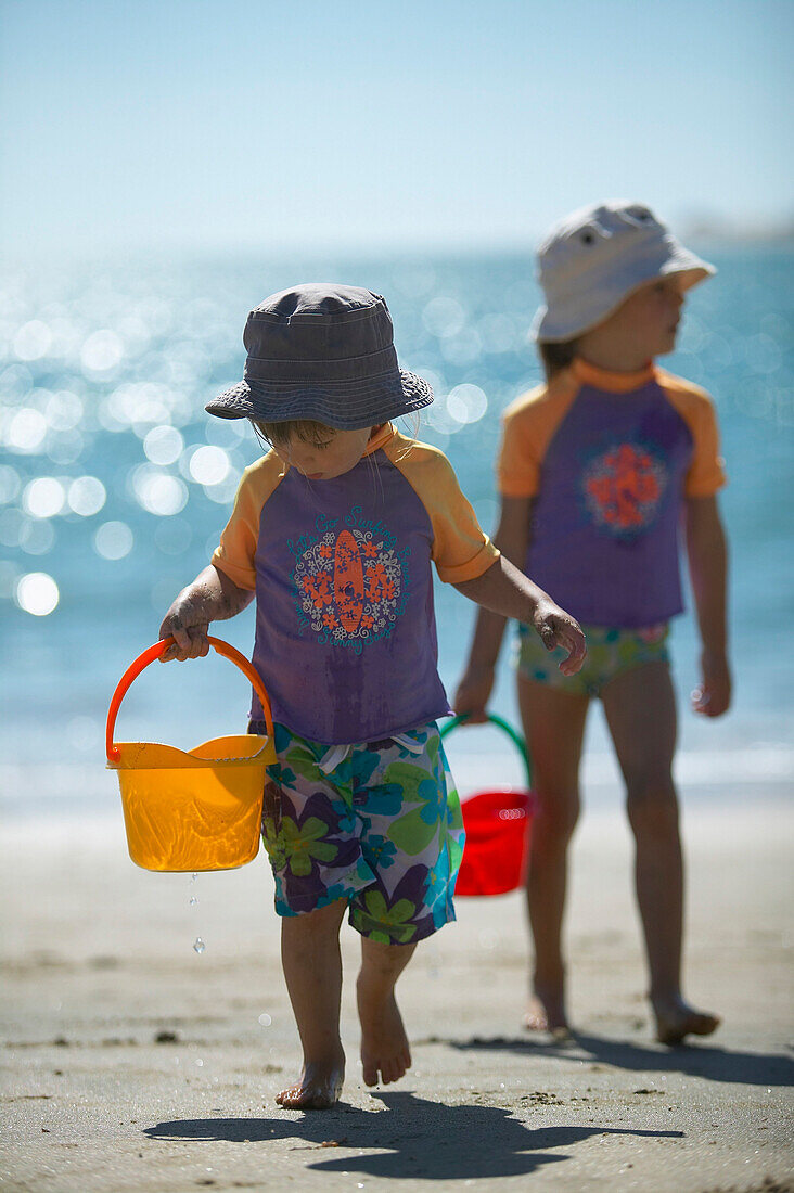 Two girls (2-5 years) carrying buckets along beach Kniepsand, Wittduen, Amrum island, North Frisian Islands, Schleswig-Holstein, Germany
