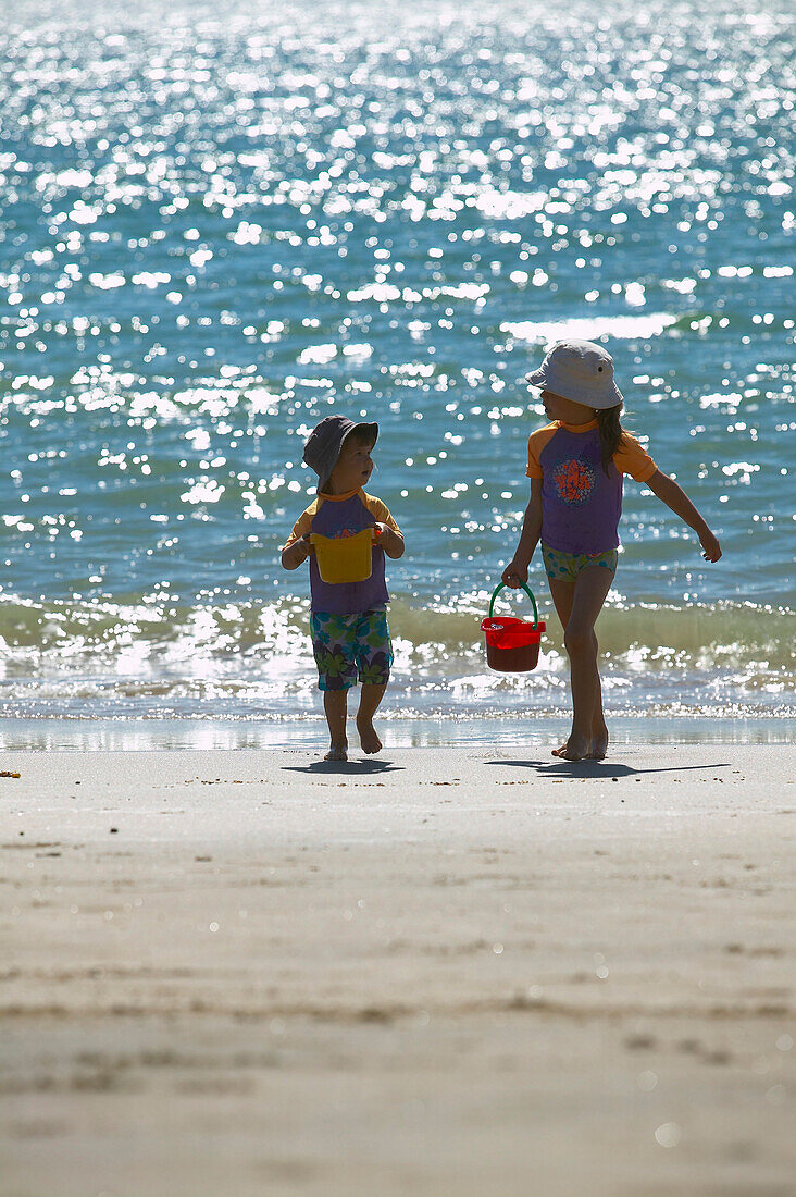 Two girls (2-5 years) carrying buckets along beach Kniepsand, Wittduen, Amrum island, North Frisian Islands, Schleswig-Holstein, Germany