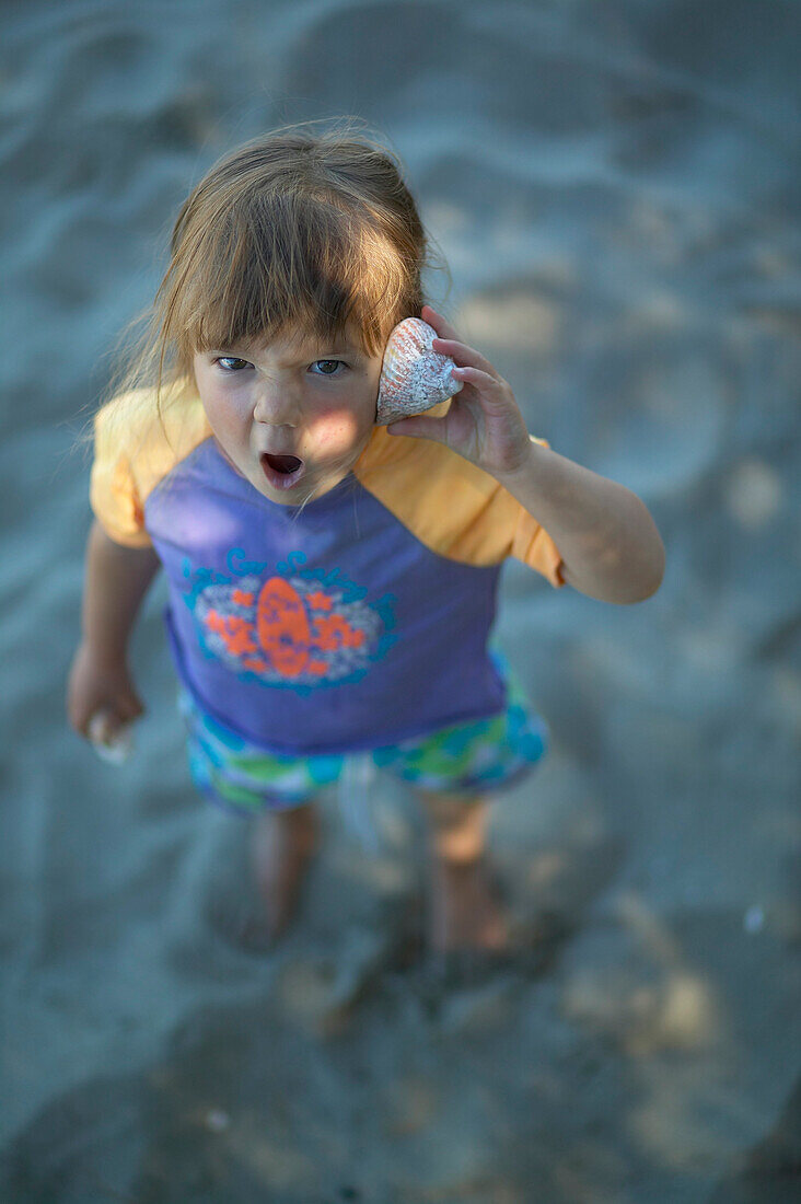 Mädchen horcht an gefundener Muschel, Strand in Pakawau, Golden Bay, Nordküste, Südinsel, Neuseeland