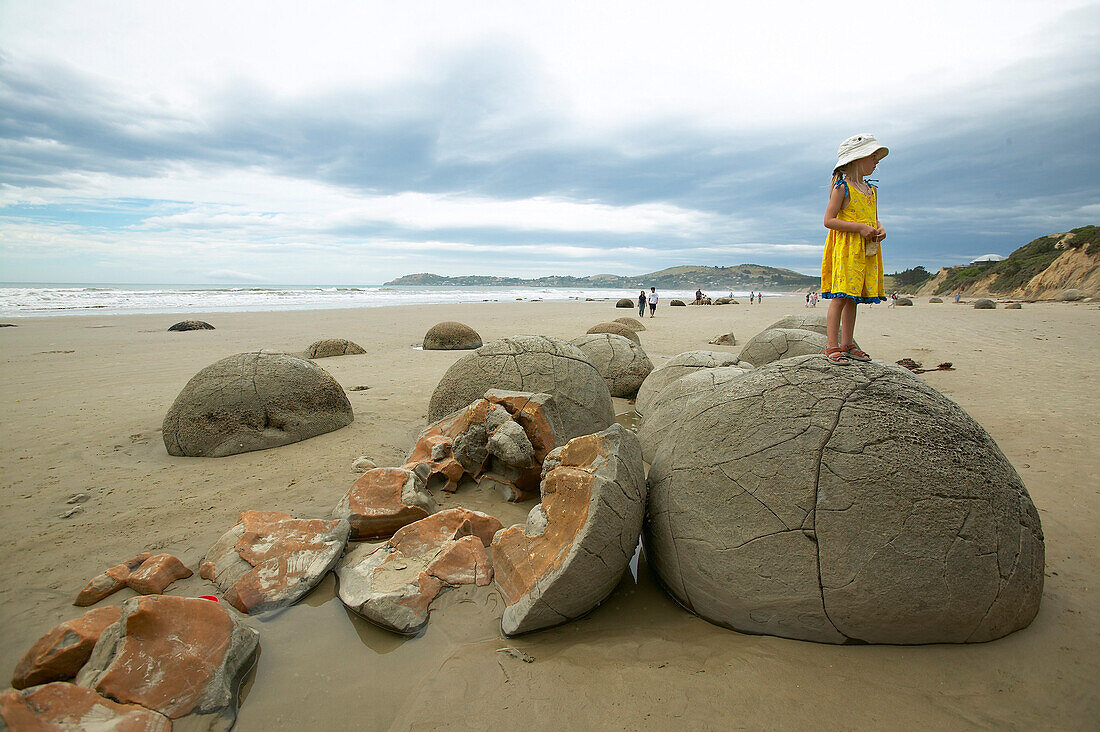 Girl standing on stone boulders, beach at the Moeraki Boulders, south of Oamaru, Eastcoast, South Island, New Zealand
