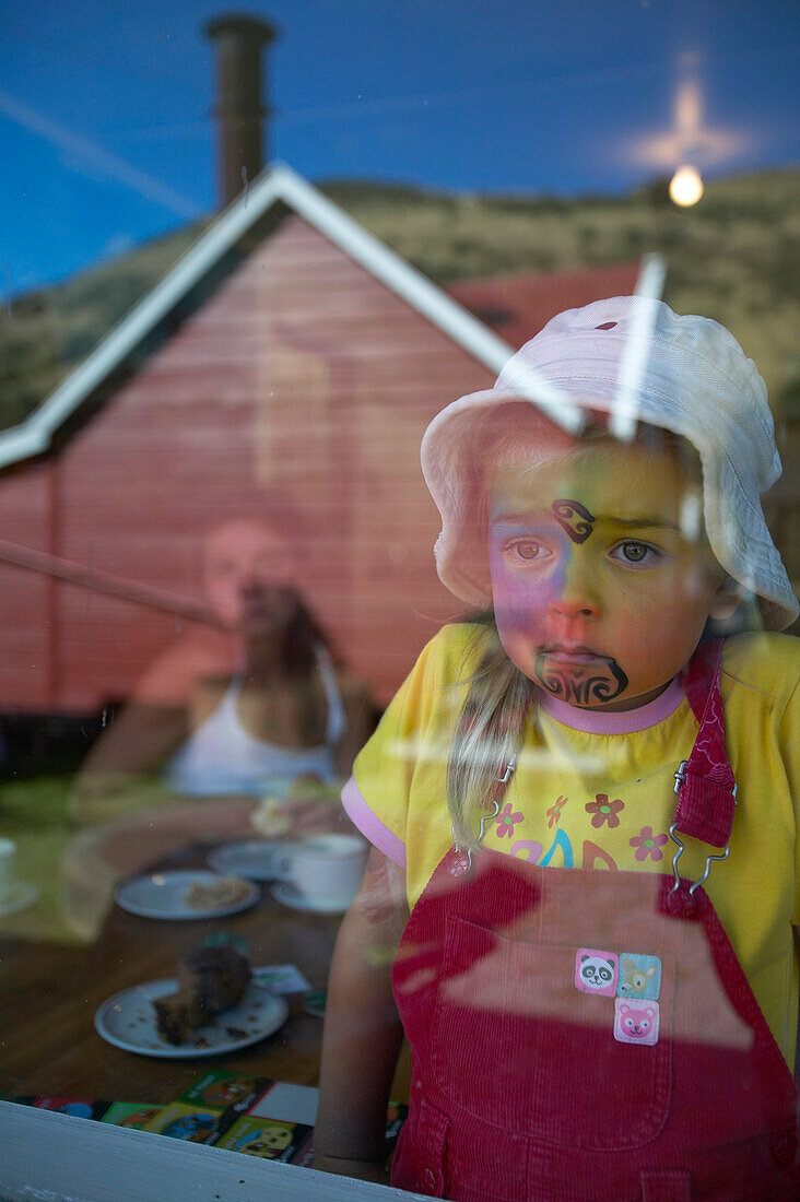 Mädchen mit Facepainting, nachempfundenes Moko, (Maori Gesichtstatoo),  Spiegelung im Café, Feier am Waitangi Day, Okains Bay, Bank's Peninsula, Ostküste, Südinsel, Neuseeland