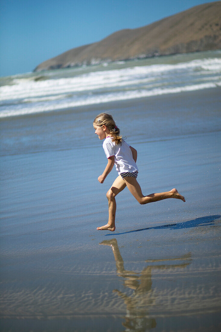 Girl running at the beach of Little Okains Bay at low tide, Okains Bay, Bank`s Peninsula, east coast, South Island, New Zealand
