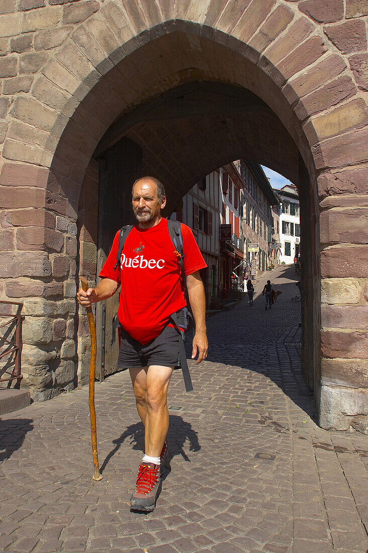 A man, pilgrim walking through the city gate, St. James Way, St. Jean-Pied-de-Port, Euskadi, Pyrenees, Department Pyrénées-Atlantiques, France