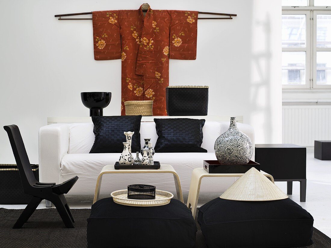 Black chair and seat cushion with white sofa around a side table with a kimono hanging on the wall