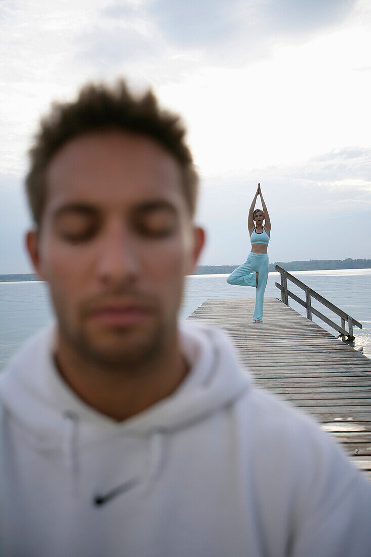 Mann mit geschlossenen Augen, Frau beim Yoga auf Steg am Starnberger See, Münsing, Bayern, Deutschland, MR