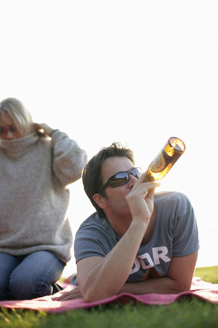 Man lying on blanket while drinking a bottle of beer, Ambach, Lake Starnberg, Bavaria, Germany