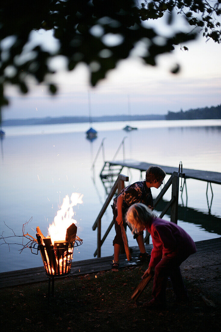 Zwei Kinder stehen rund ums Feuer, abenddämmerung, Worthsee, Oberbayern, Bayern, Deutschland