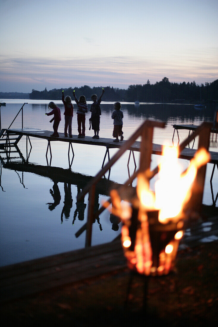 Kinder auf einem Holzsteg am Wörthsee, Lagerfeuer im Vordergrund, Bayern, Deutschland, MR