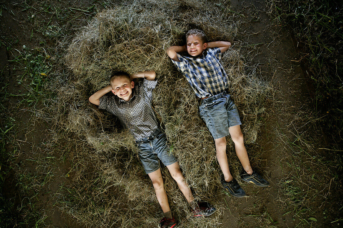 Zwei Jungen (8-9  Jahre) liegen im Heuhaufen, Walchstadt, Oberbayern, Bayern, Deutschland, MR