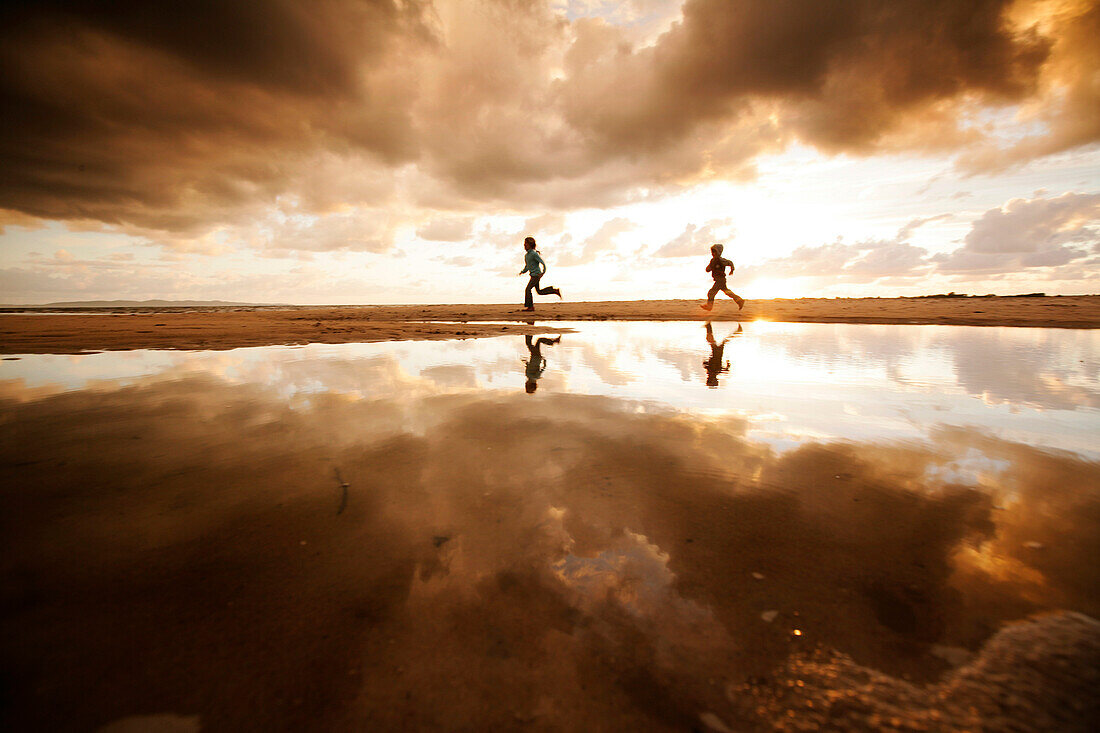 Zwei Kinder laufen am Strand, Spiegelung von Wolkenhimmel im Wasser, Segeltorpstrandet, Halmstadt, Skane, Schweden