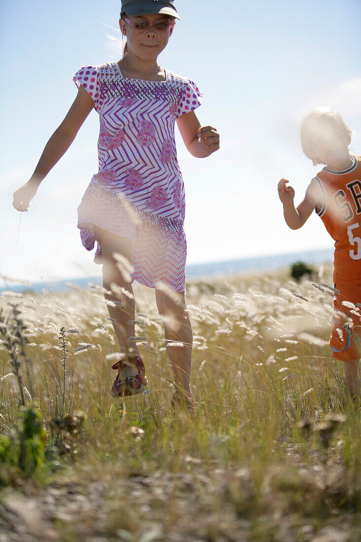 Boy and girl running through meadow of shore grass, Sysne, Gotland, Sweden