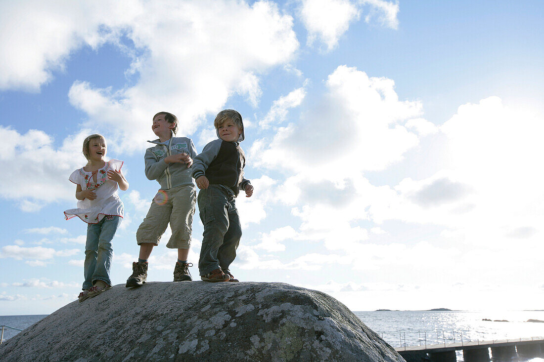 Three Kids standing on a big boulder, stone, on the beach, Torekov, Skane, Sweden