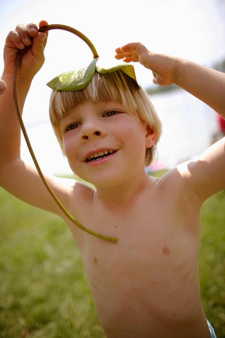 Junge (4-5 Jahre) mit einem Seerosenblatt auf dem Kopf, Staffelsee, Oberbayer, Bayern, Deutschland