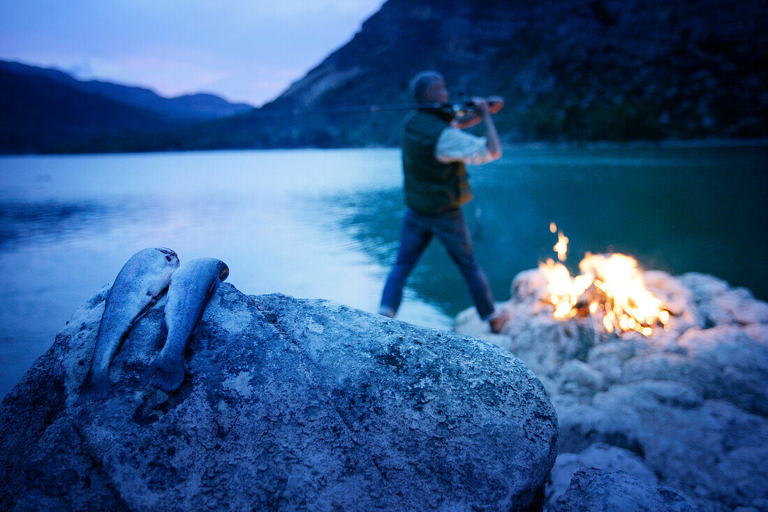 Mann beim Fischen am Lagerfeuer in der Dämmerung, Stausee, Valencia, Spanien