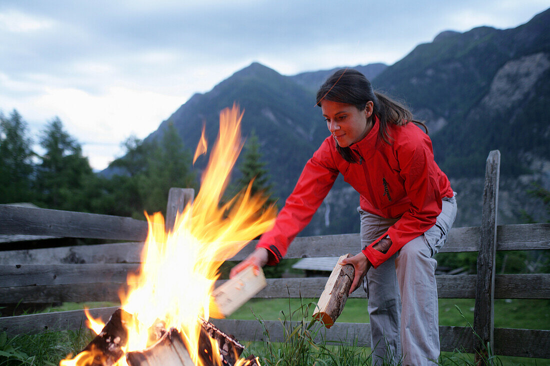 Frau legt Holz auf ein Lagerfeur, Heiligenblut, Nationalpark Hohe Tauern, Kärnten, Österreich