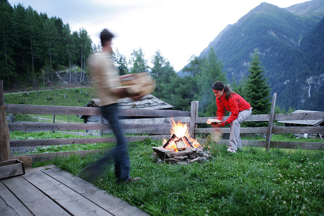 Junge Leute vor einer Almhütte, Lagerfeuer im Vordergrund, Heiligenblut, Nationalpark Hohe Tauern, Kärnten, Österreich