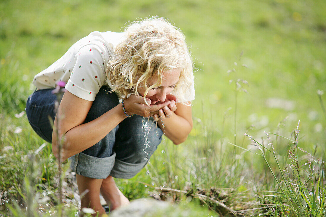 Frau trinkt Wasser am Bach, Heiligenblut, Nationalpark Hohe Tauern, Kärnten, Österreich