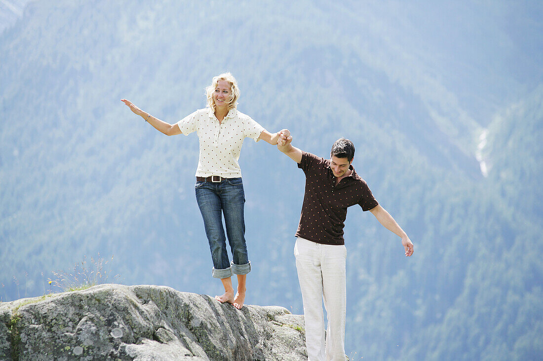 Young couple balancing over rock, Heiligenblut, Hohe Tauern National Park, Carinthia, Austria