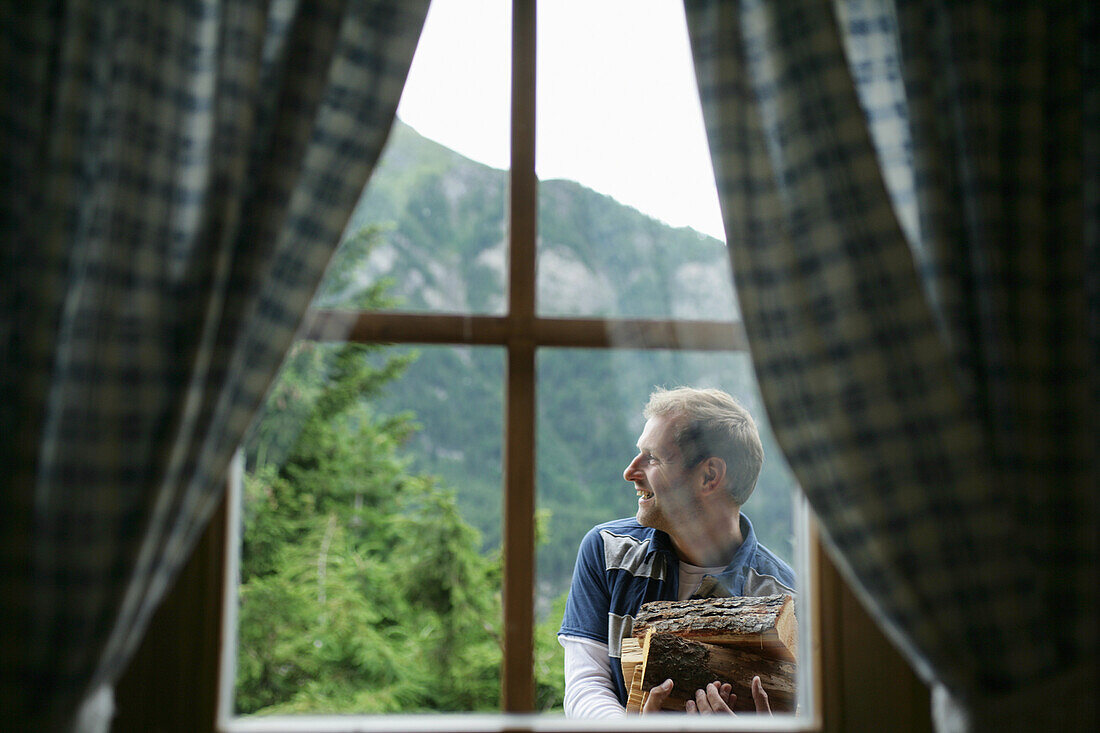 Blick aus einer Almhütte auf einen Mann mit Holzscheiten, Heiligenblut, Nationalpark Hohe Tauern, Kärnten, Österreich