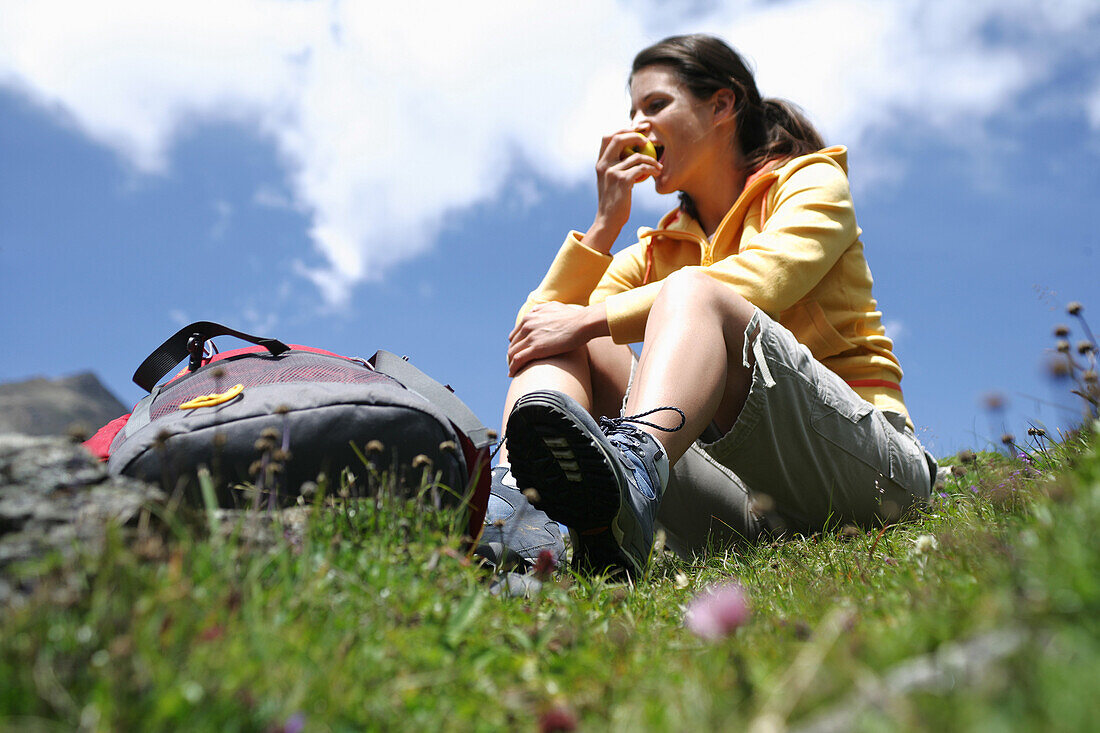 Woman sitting on grass while eating an apple, Heiligenblut, Hohe Tauern National Park, Carinthia, Austria