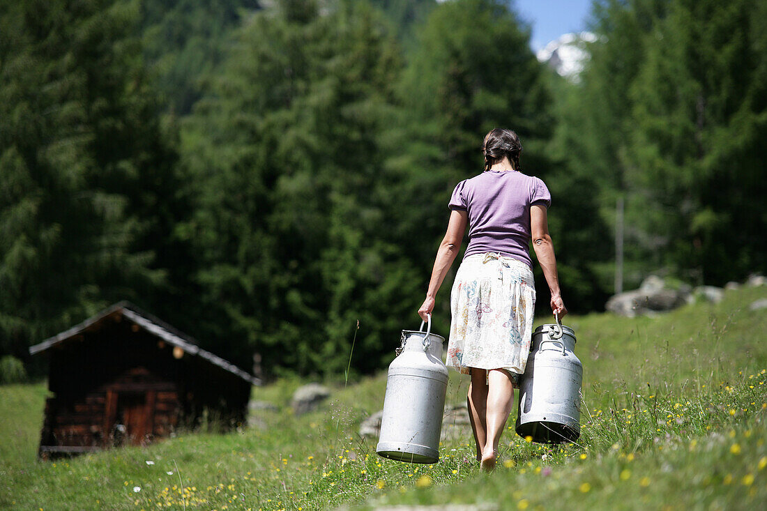 Woman carrying milk cans on alp, Heiligenblut, Hohe Tauern National Park, Carinthia, Austria