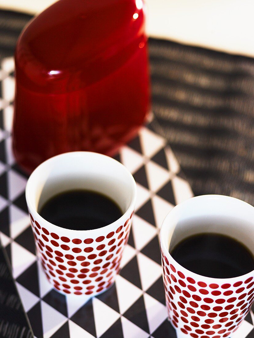 Gefüllte Kaffeebecher und rote Dose auf schwarz weiss gemustertem Untergrund