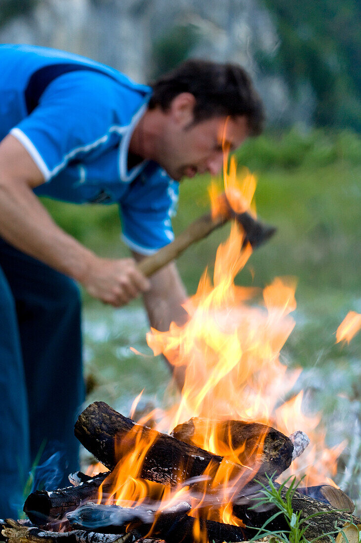 Mann hackt Holz, Lagerfeuer im Vordergrund, Sarcatal, Trention, Trentino-Südtirol, Italien