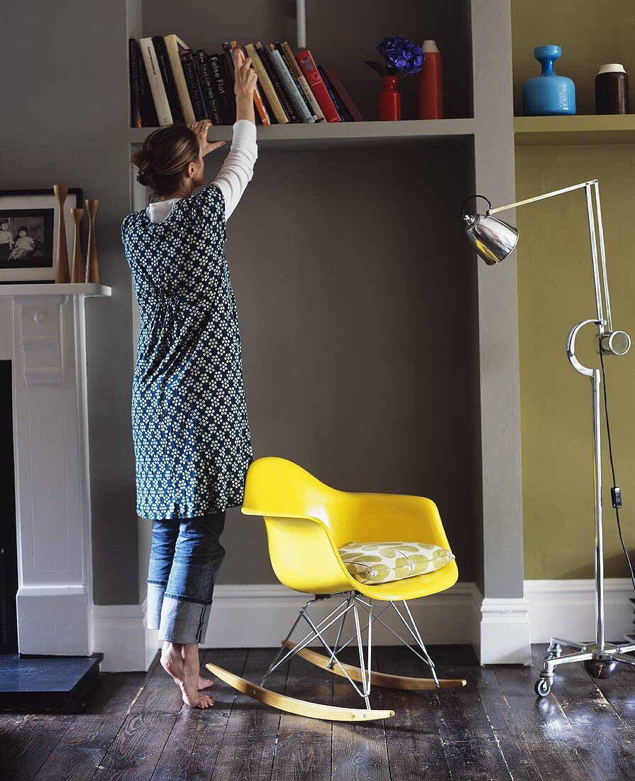 A plastic rocking chair, a floor lamp on wheels and a woman in front of a bookshelf