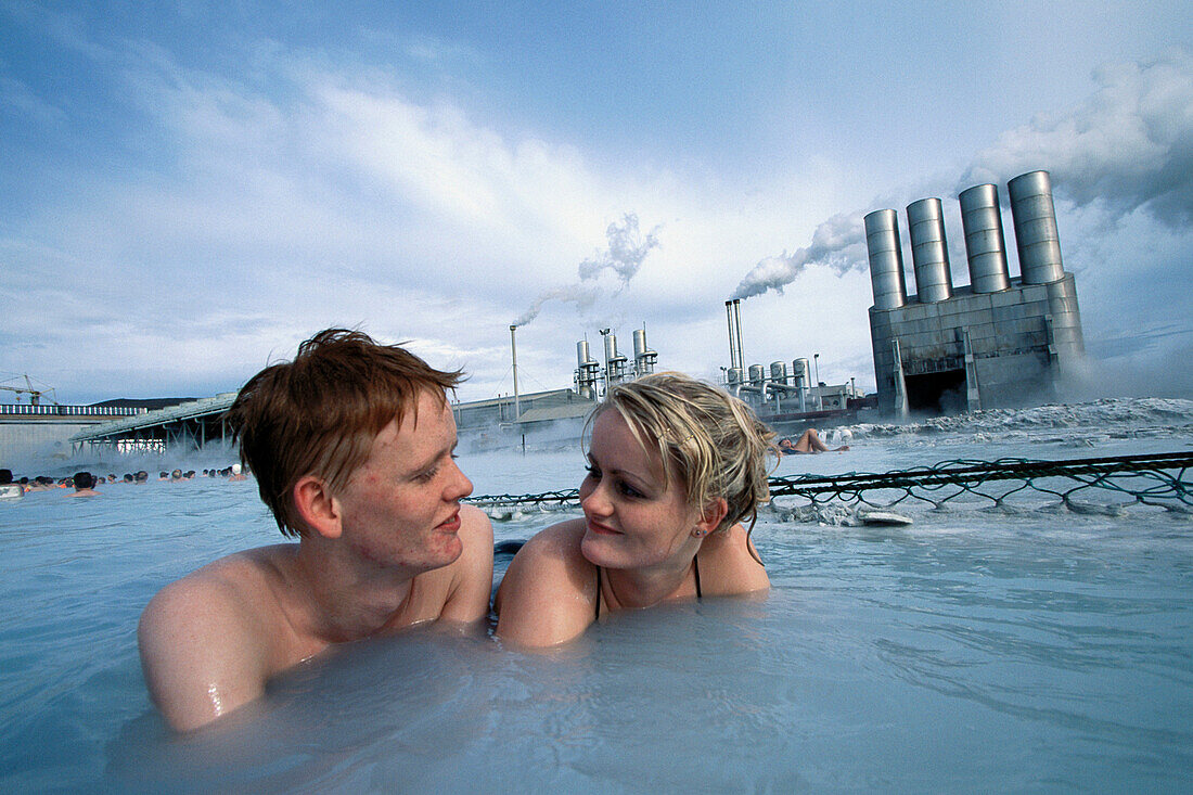 Couple in swimming pool. Geothermal power plant in background. The Blue Lagoon. Grindavik. Iceland