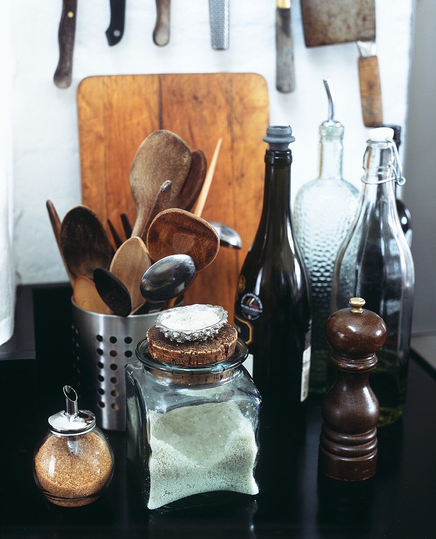 A pepper mill, a jar of salt, brown sugar in a shaker, wooden spoons etc