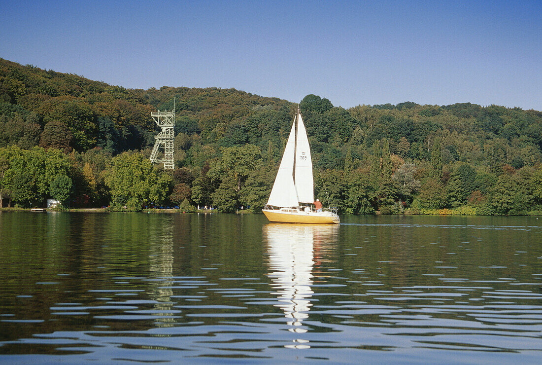 A sailing boat on a lake with a shaft tower in the background, Baldeney Lake, Essen, Ruhr Valley, Ruhr, Northrhine, Westphalia, Germany