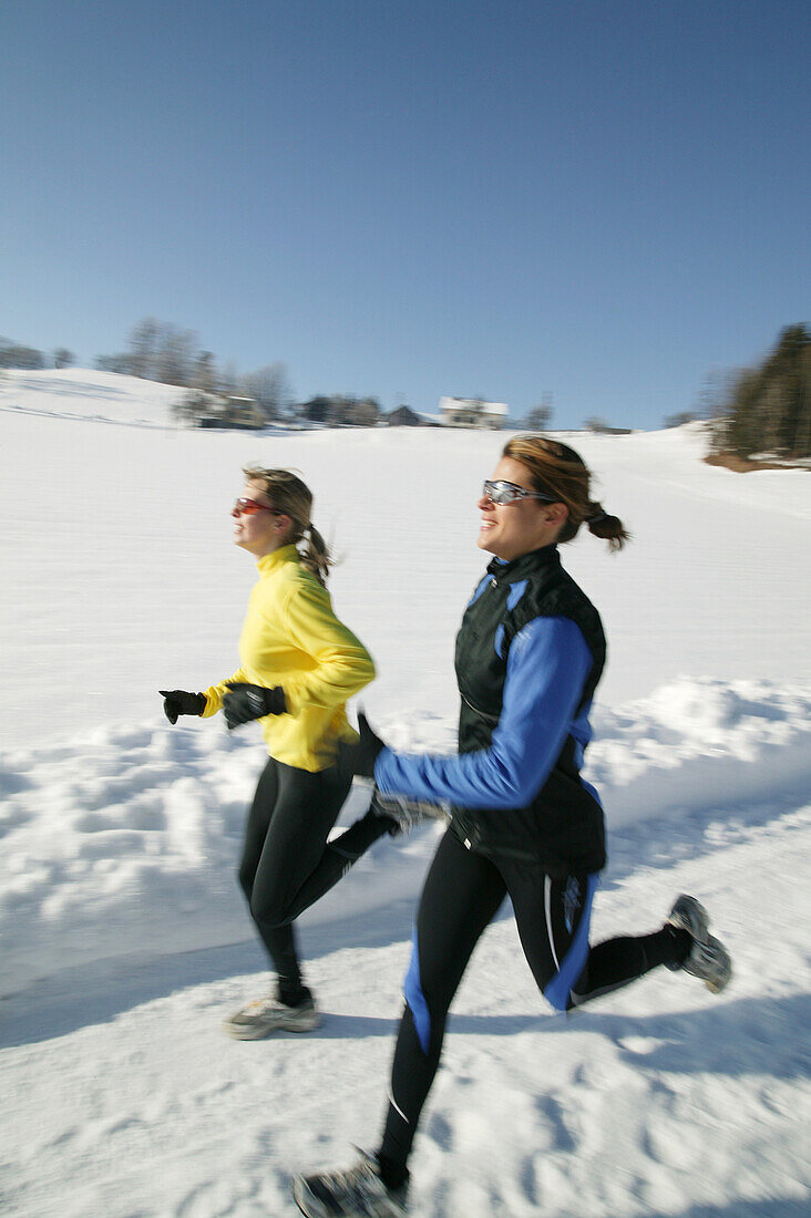 Zwei Frauen joggen über verschneiten Weg, Steiermark, Österreich