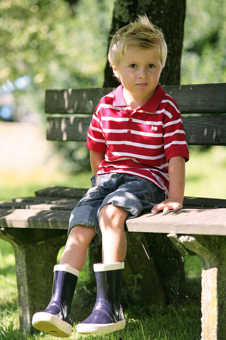 Junge (4-5 Jahre) sitzt auf einer Gartenbank, Steiermark, Österreich