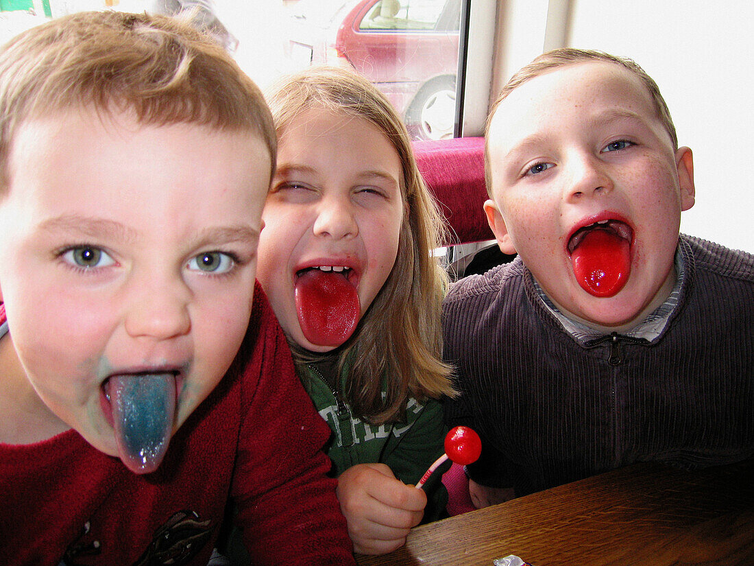 Three boys, aged 4 and 8, show off their colored tongues while sucking on flavoured lollipops
