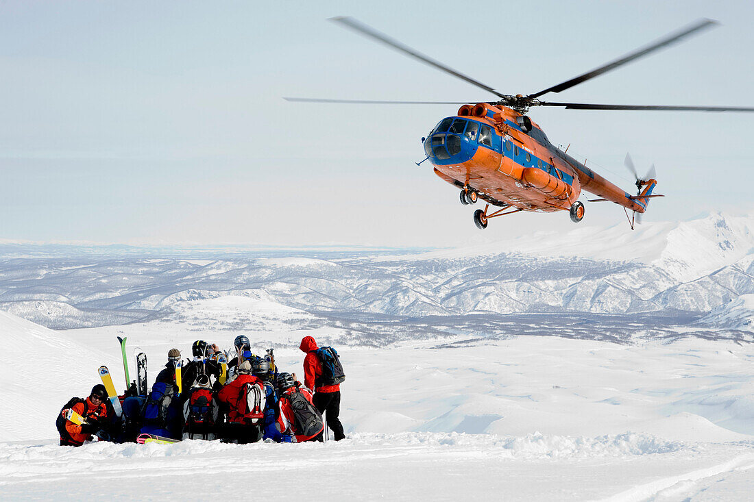 Helicopter picking up a group of skiers in snow, Heliskiing, Kamchatka Peninsula, Sibiria, Russia