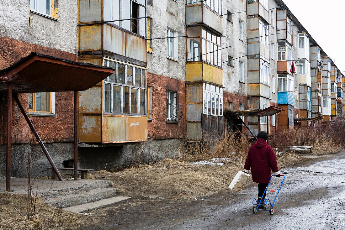 Yelizovo, Elizovo, nahe Petropavlovsk, Kamtschatka, Sibirien, Russland, Frau läuft vor einer verwitterten Plattenbausiedlung.