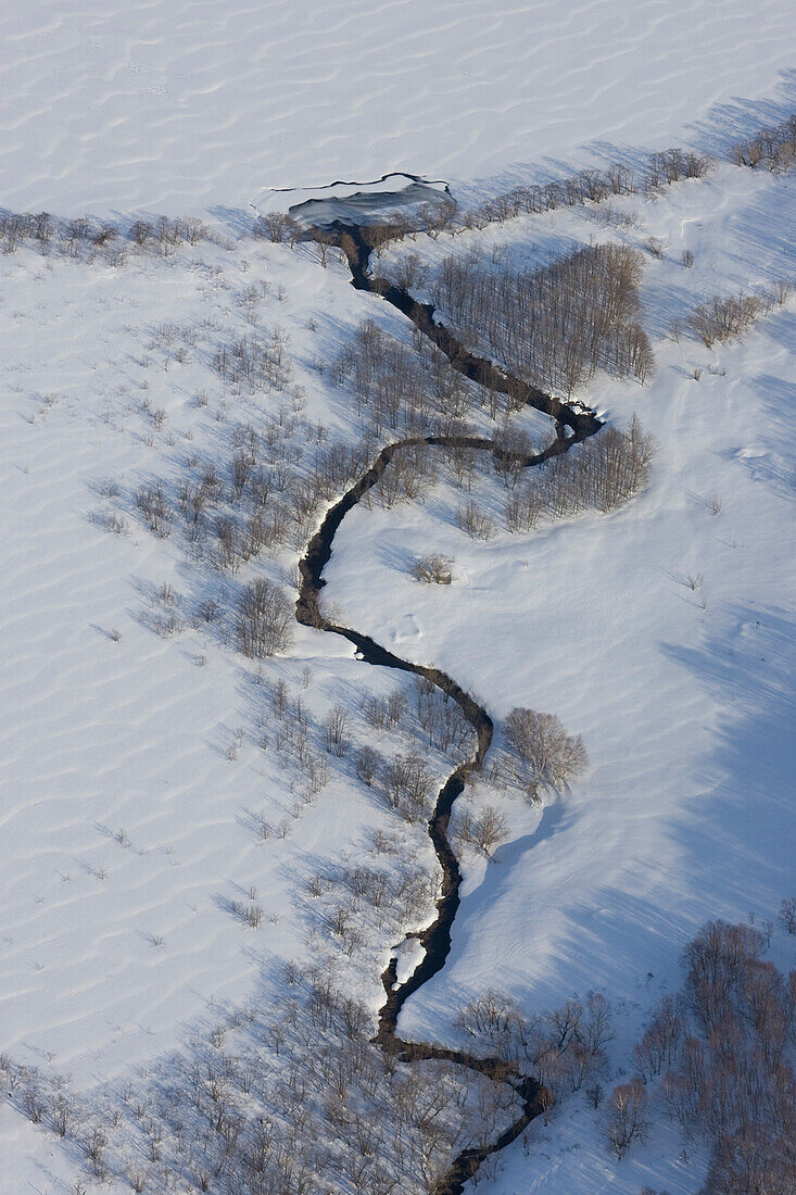 Kamtschatka, Sibirien, Russland, ein Flüsschen mäandriert durch eine verschneite Landschaft und fliesst in einen zugefrorenen See, Luftaufnahme