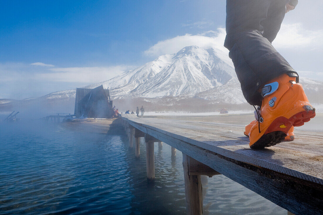 Person wearing ski boots walking over wooden bridge, Kamchatka Peninsula, Sibiria, Russia