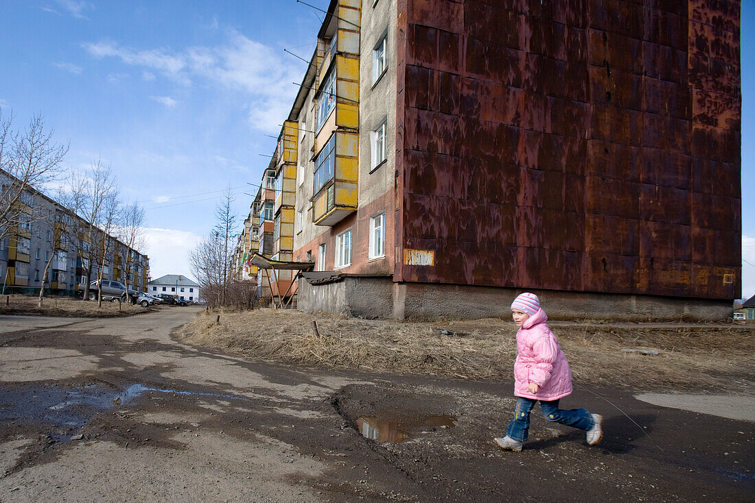 Yelizovo, Elizovo nahe Petropavlovsk, Kamtschatka, Sibirien, Russland, ein kleines Mädchen, ein Kind spielt vor einer verwitterten Plattenbausiedlung.