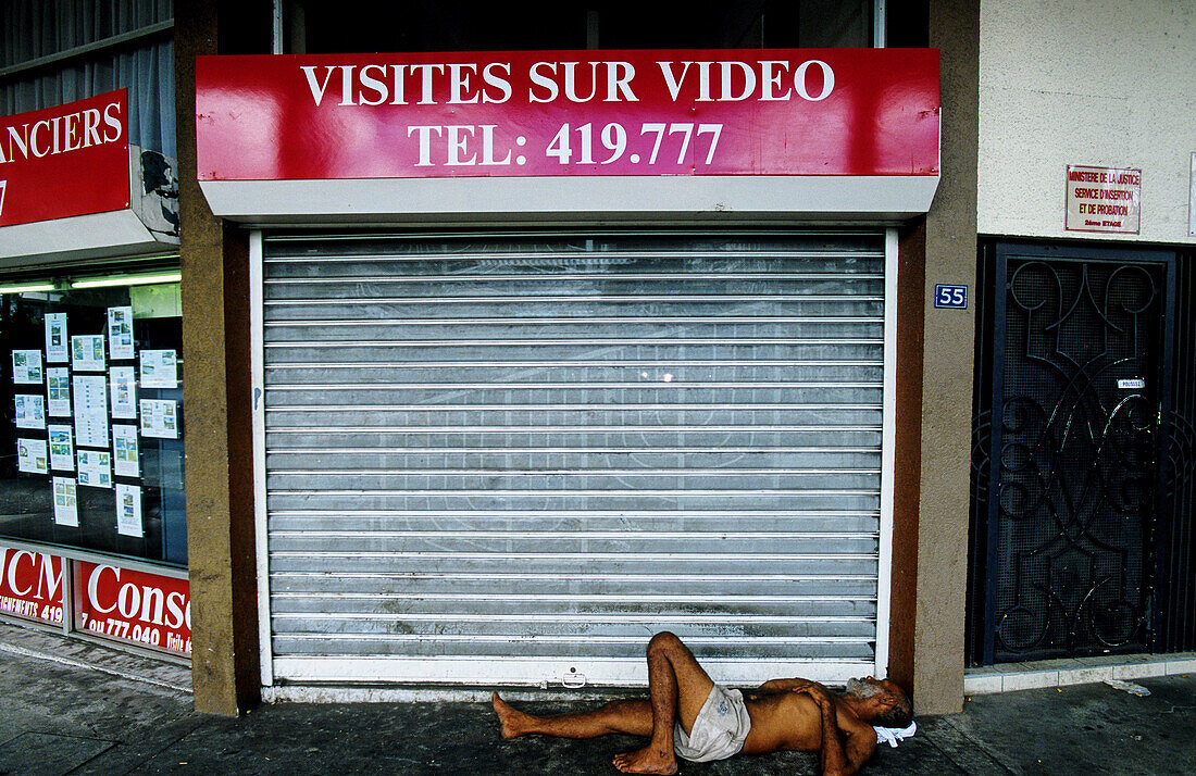 Drunk homeless lying down by a shop window. Papeete. Tahiti island in the Windward islands. Society archipelago. French Polynesia