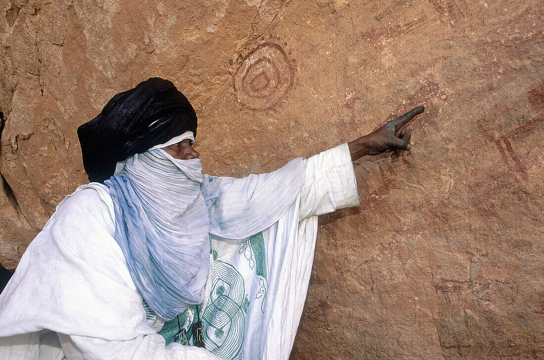 Tuareg pointing out prehistoric drawings in a natural cave. Tassili N Ajjer desert. Algeria