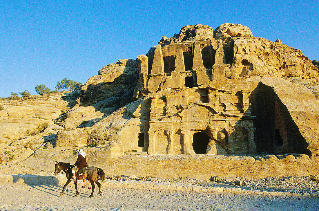 Graves carved in the rock and Bedouin rider at fore, archeological site of Petra. Jordan