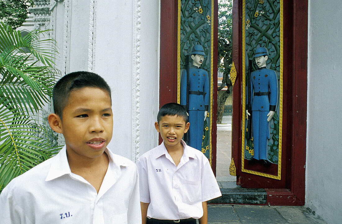 Children at carved gates of Wat Ratchabophit Buddhist temple. Bangkok. Thailand