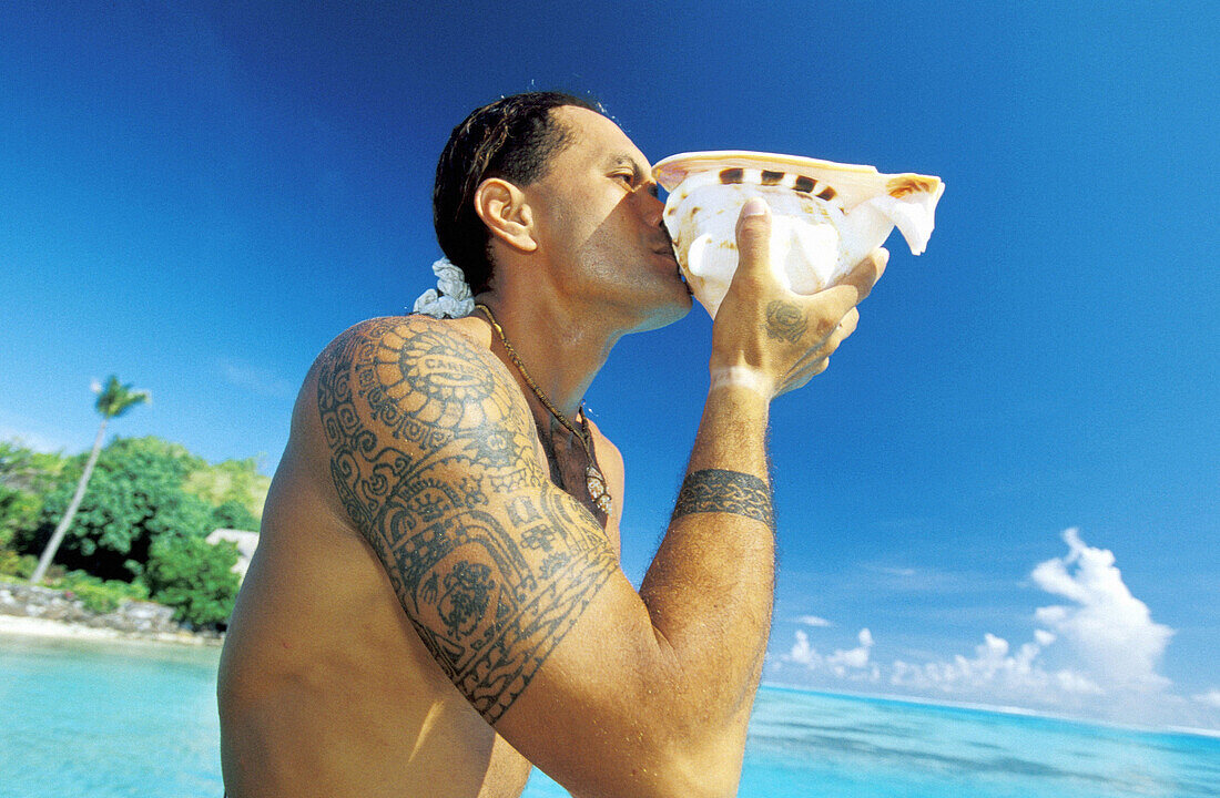 Tattoed young man blowing in a seashell. Bora Bora, Leeward Islands. French Polynesia