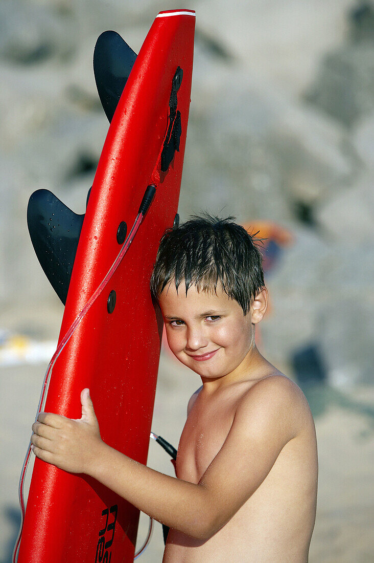 8-jähriger Junge mit Surfbrett am Strand, Hendaye. Aquitaine, Frankreich